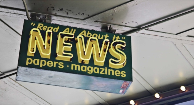 neon sign hanging from ceiling that says "read all about it - news - papers - magazines"